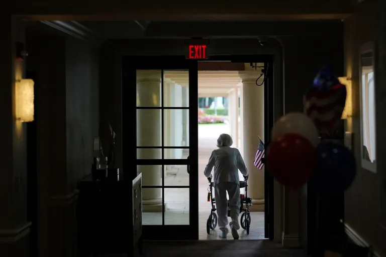 A woman uses a walker as she exits an assisted living building