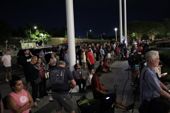 People wait for President Donald Trump's name to be removed from the John F. Kennedy Center for the Performing Arts in Washington, Friday, June 12, 2026. 