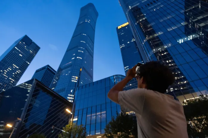 A passerby tries to take photo of the damage on the Citic Tower also known as Zun Tower in Beijing, China, Friday, June 26, 2026. (AP Photo/Han Guan Ng)