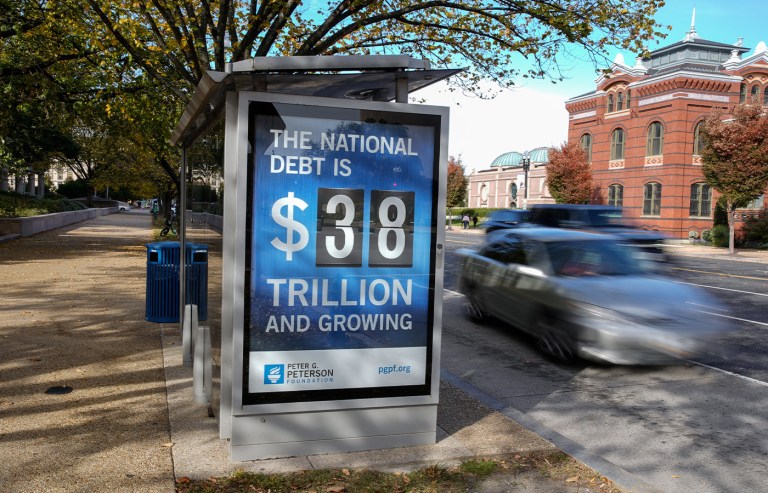 A bus shelter displays an electronic billboard and a poster showing the current U.S. National debt in Washington, D.C. in October 2025. As of press time, the national debt stands at over $39.2 billion. (Jemal Countess/Getty Images for the Peter G. Peterson Foundation)