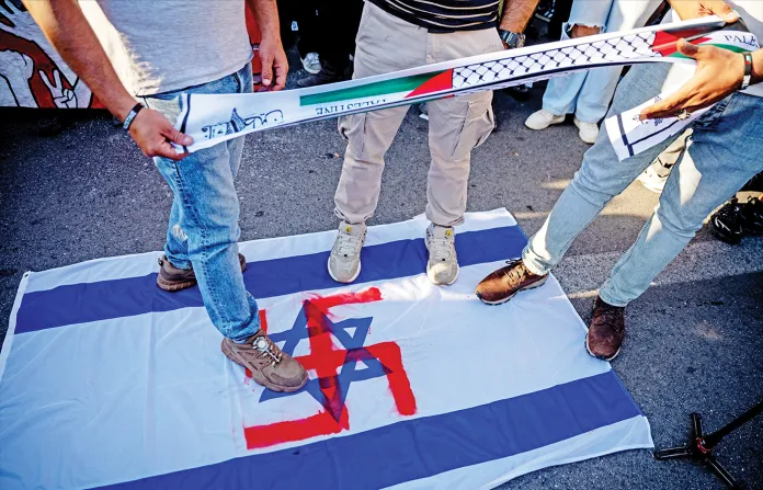 Protesters in Athens stand on an Israeli flag defaced with a swastika, May 18, 2026. (Aggelos NAKKAS / AFP / Getty Images)