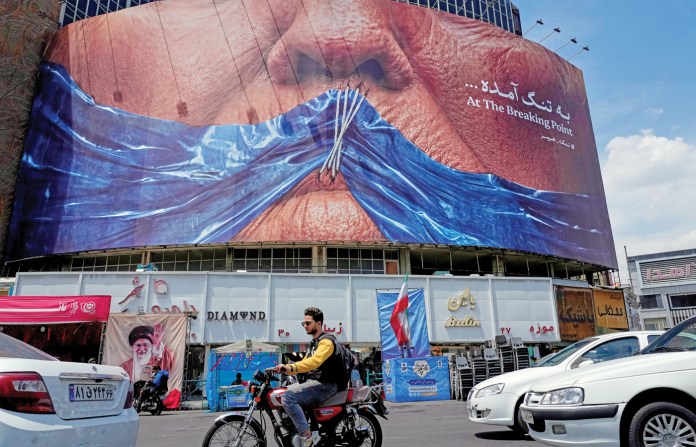 Drivers in Tehran pass a billboard showing the Strait of Hormuz and the sewn lips of U.S. President Donald Trump, May 2, 2026. (Vahid Salemi/AP)