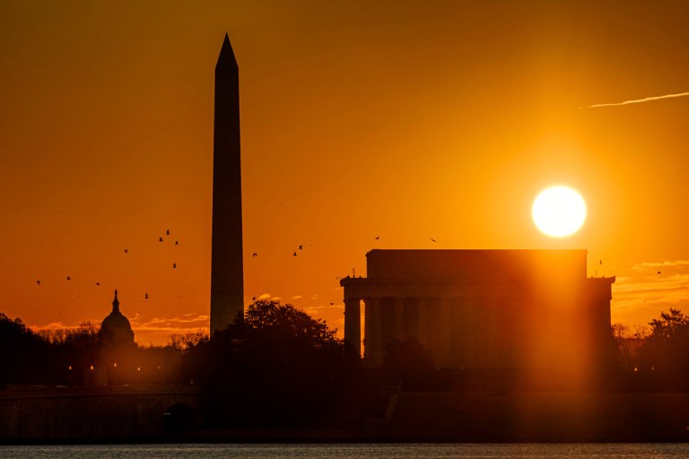 The sun rises above the Lincoln Memorial with the Washington Monument and the U.S. Capitol in the background.