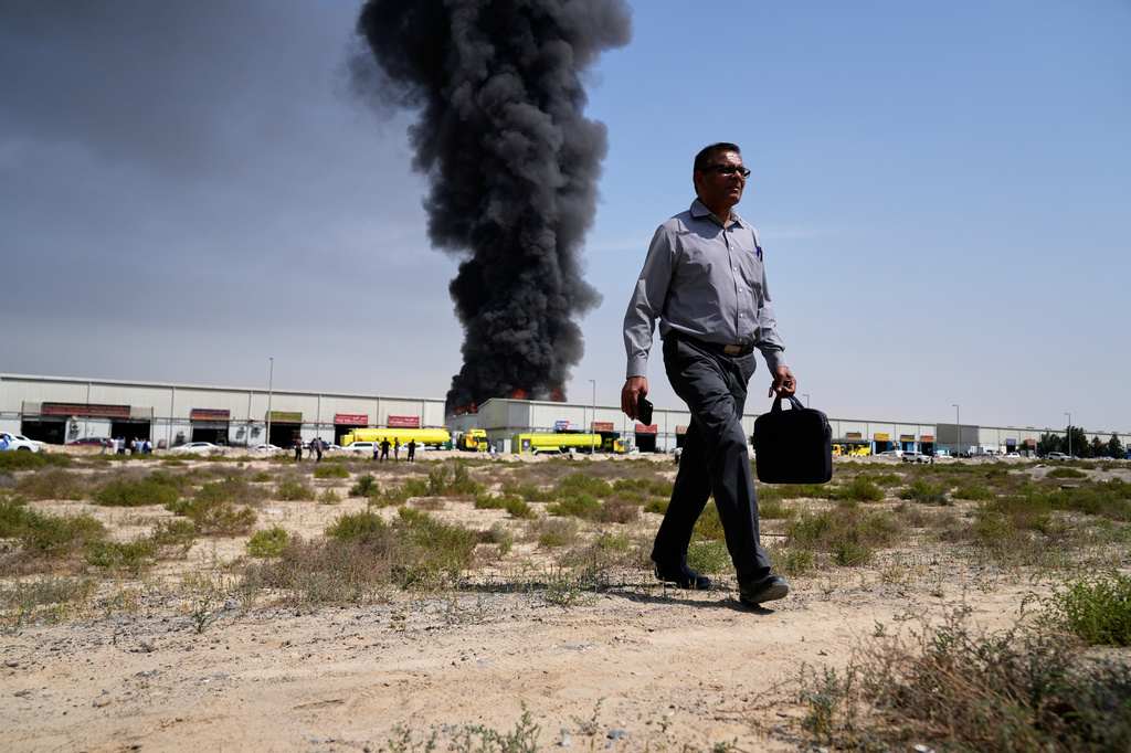 A man walks away after watching as a black plume of smoke rises from a warehouse in the industrial area of Sharjah City, United Arab Emirates, March 1, 2026, following reports of Iranian strikes in Dubai. (AP Photo/Altaf Qadri)