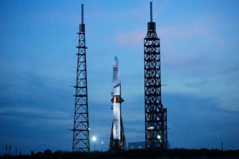 A Blue Origin New Glenn rocket stands ready for launch against an ocean-blue sky.