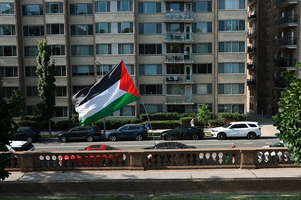WASHINGTON, DC - JULY 02: A protester carries a Palestinian flag near Meridian Hill Park before an event with members of the U.S National Guard and U.S. Secretary of War Pete Hegseth on July 02, 2026 in Washington, DC. Hegseth and other members of U.S. President Donald Trump's administration visited the park to speak to guard members and to tout the DC Safe And Beautiful Task Force.