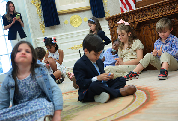 Children sit on the floor of the Oval Office and sleep against the Resolute Desk as U.S. President Donald Trump speaks during an event to mark the first day of trading for "Trump Accounts" at the White House on July 06, 2026 in Washington, DC. The accounts are a $1,000 government seed deposit for children born between 2025 and 2028, with family and employer contributions capped at $5,000 annually and restricted to low-cost U.S. equity index funds. 