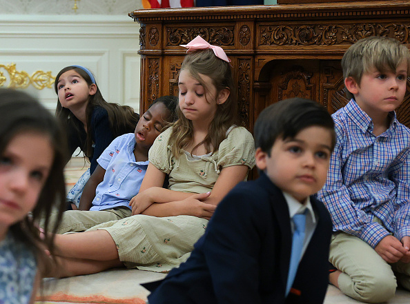 WASHINGTON, DC - JULY 06: Children sit on the floor of the Oval Office and sleep against the Resolute Desk as U.S. President Donald Trump speaks during an event to mark the first day of trading for "Trump Accounts" at the White House on July 06, 2026 in Washington, DC. The accounts are a $1,000 government seed deposit for children born between 2025 and 2028, with family and employer contributions capped at $5,000 annually and restricted to low-cost U.S. equity index funds. 