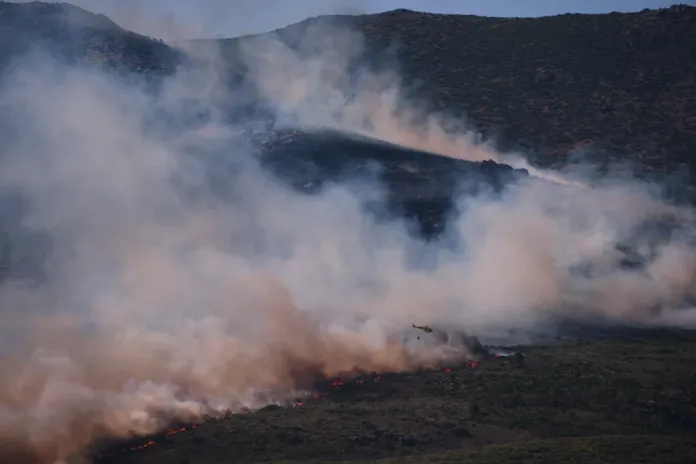 A firefighting helicopter drops water on a wildfire