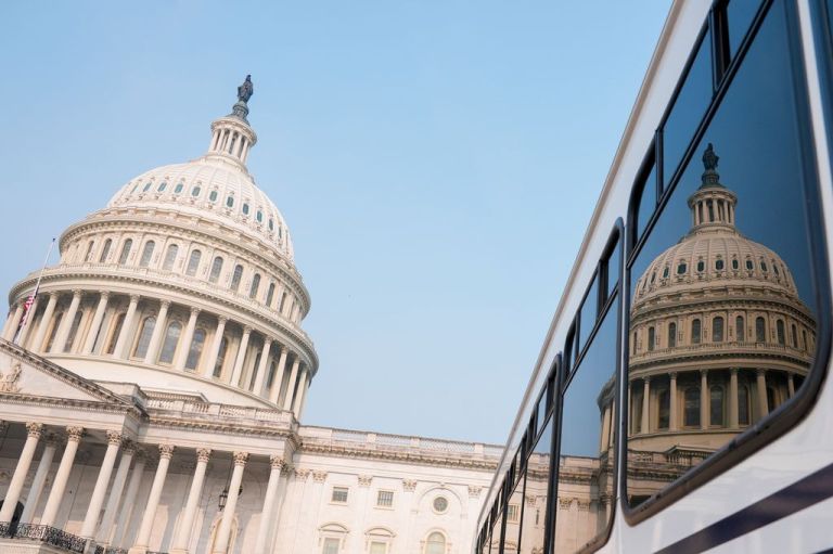 The U.S. Capitol with a glass building, right, reflecting it to show a mirror image of the building.