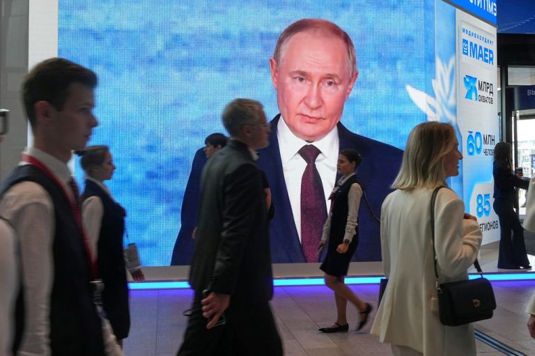 People walk past a screen with an image of Russian President Vladimir Putin.