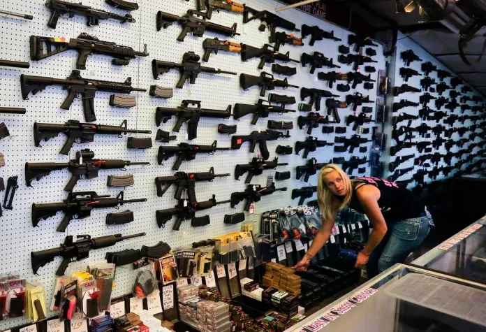With guns displayed for sale behind her, a gun store employee helps a customer at Dragonman's, east of Colorado Springs, Colo.