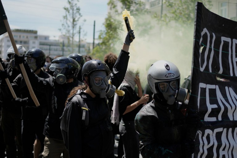A protester from the anarchist block wearing helmet and tear gas mask, holds a smoke flare during a May Day rally in Athens, Greece, Thursday, May 1, 2025.