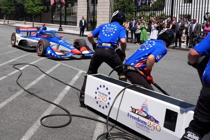 David Malukas drives a race car as a pit crew prepares to demonstrate a tire change