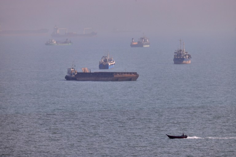 A small boat sails past cargo ships and other commercial vessels anchored in the Strait of Hormuz.