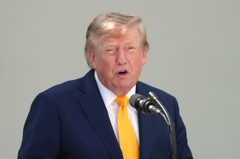 President Donald Trump speaks into a microphone with a yellow tie on at the White House.