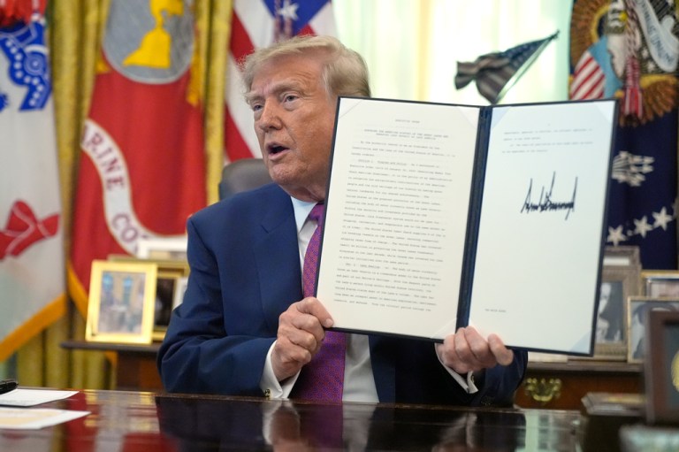 President Donald Trump holds up a signed executive order in the Oval Office.