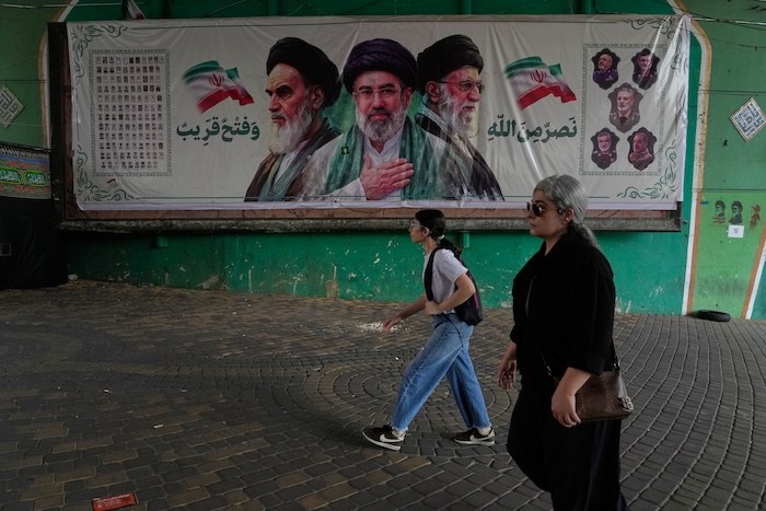Women walk past a banner showing portraits of Ayatollah Ruhollah Khomeini, supreme leader Mojtaba Khamenei and Ayatollah Ali Khamenei.