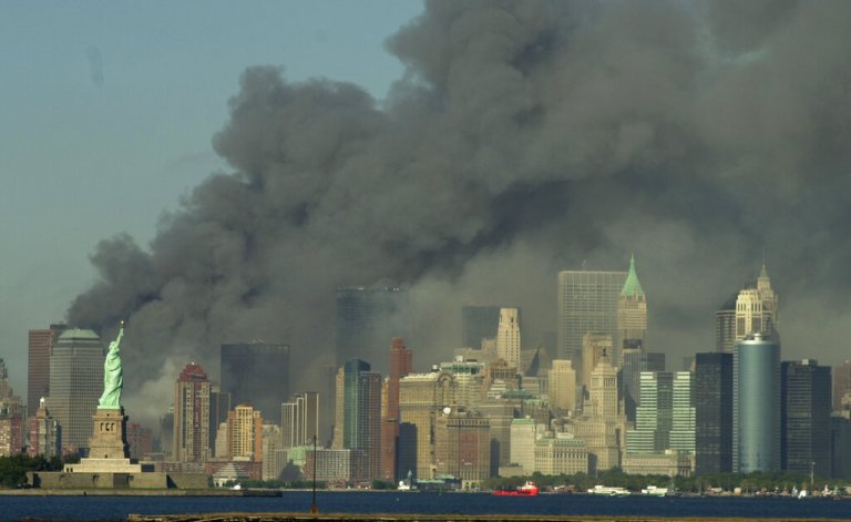 Thick smoke billows into the sky from the area behind the Statue of Liberty, lower left, where the World Trade Center towers stood, on Tuesday, Sept. 11, 2001. The towers collapsed after terroists crashed two planes into them.