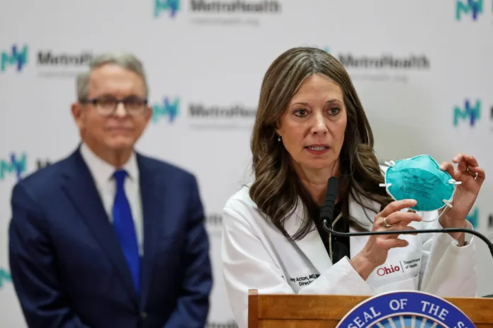 FILE - Ohio Department of Health Director Amy Acton holds up a mask as she gives an update at MetroHealth Medical Center as Ohio Gov. Mike DeWine, listens, Feb. 27, 2020, in Cleveland, on the state's preparedness and education efforts on COVID-19. (AP Photo/Tony Dejak, File)