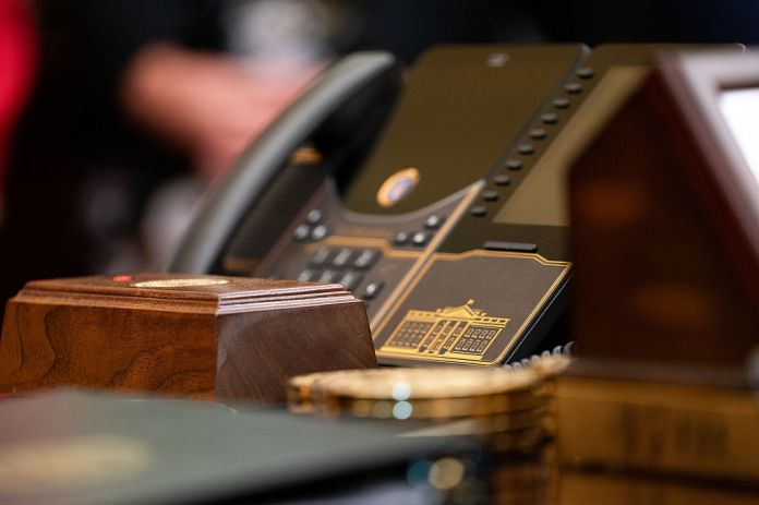 A phone with gold embellishments on the Resolute Desk during an executive order signing ceremony in the Oval Office of the White House in Washington, DC, US, on Monday, Aug. 3, 2026. The executive order establishes the Military Spouse Commission, which will be chaired by Jennifer Rauchet, wife of Defense Secretary Pete Hegseth, and is meant to provide policy recommendations that would improve the quality of life of military spouses and families.