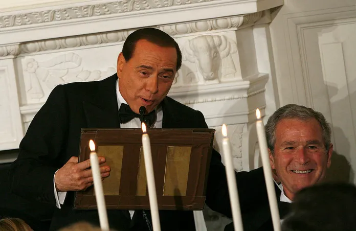 talian Prime Minister Silvio Berlusconi holds part of the podium he was speaking from that fell apart at the end of his speech as President George W. Bush laughs during an official dinner held for Berlusconi in the State Dining Room