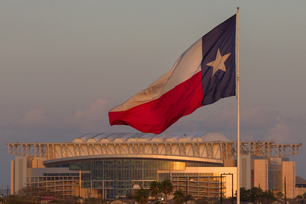 A Texas state flag waves in the wind backdropped by the NRG Stadium, one of the stadiums that will host 2026 FIFA World Cup matches, in Houston, Sunday, Dec. 28, 2025. (AP Photo/Jon Shapley)