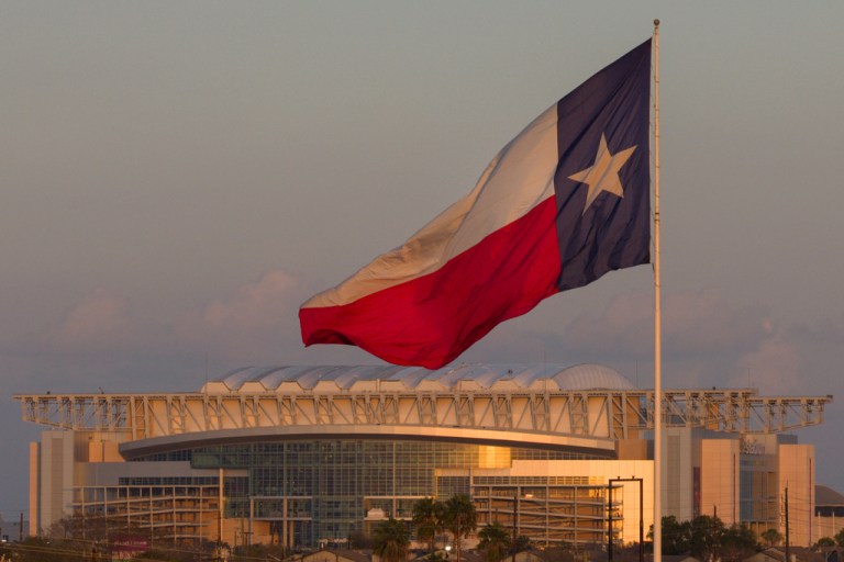 A Texas state flag waves in the wind backdropped by the NRG Stadium, one of the stadiums that will host 2026 FIFA World Cup matches, in Houston, Sunday, Dec. 28, 2025. (AP Photo/Jon Shapley)