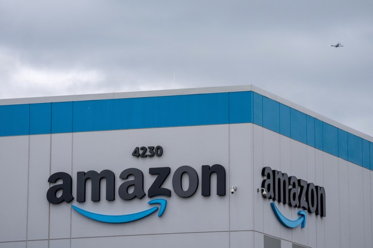A plane flies past an Amazon fulfillment center.