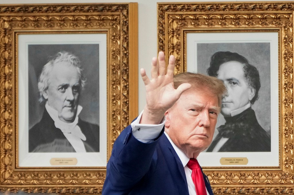 President Donald Trump waves as he walks past presidential portraits along the Colonnade.