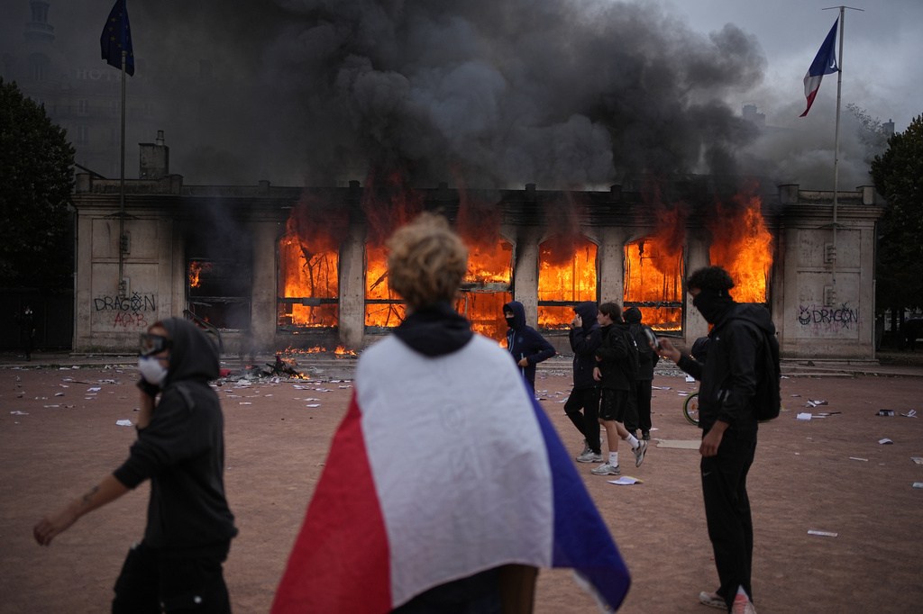 A protester wraps a French flag around them in front of a burning tourism office
