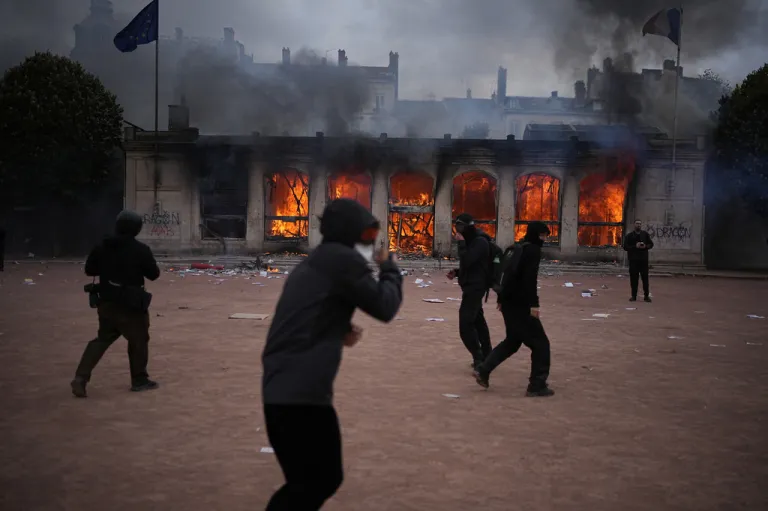 People wearing all black in Lyon, France, protest and peer at the arson of their own demise of a burning tourism office.