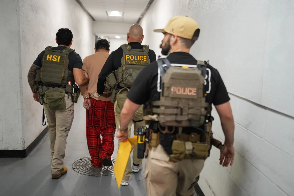 Homeland Security Investigations task force officers escort a suspect in a gray hallway accused of illegally registering to vote to a processing facility at the Federal Building in Los Angeles, Monday, Oct. 19, 2026.