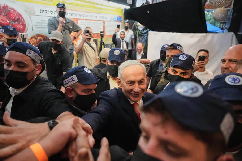 Israeli Prime Minister Benjamin Netanyahu gestures to supporters as security personnel surround him during a campaign appearance.