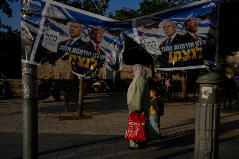 An Arab woman walks with a child next to a torn Likud party campaign ad featuring Israeli Prime Minister Benjamin Netanyahu and U.S. President Donald Trump.