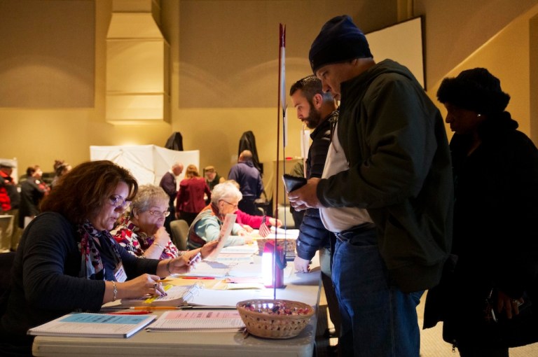Paula Dobens, an assistant election official, left, checks the id of a voter lining up to cast a ballot at a polling site for the New Hampshire primary Tuesday, Feb. 9, 2016, in Nashua, N.H.