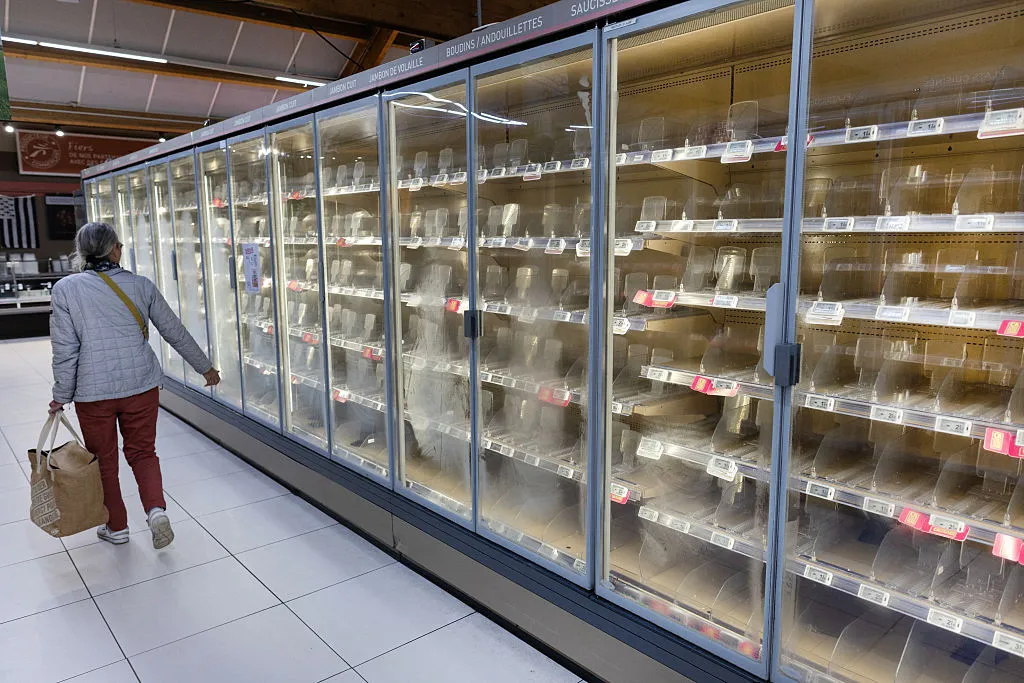 A woman walks past empty fresh-food refrigerators