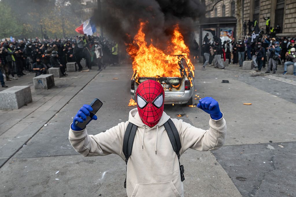 A protester dressed as Spiderman gestures as a car burns during a demonstration at Place de Republique.