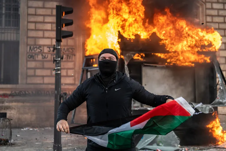 A protester holds a Palestinian flag as a bus stop burns during a demonstration at Place de Republique on October 17, 2026 in Paris, France. (Guy Smallman/Getty Images)